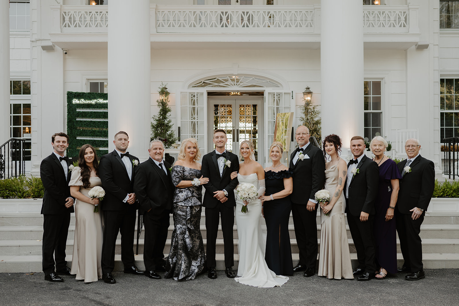 Bride and groom pose for a formal family portrait on the mansion steps, surrounded by parents and relatives.